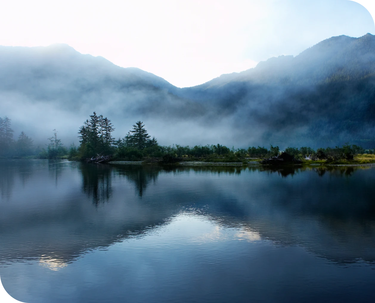 Foggy mountain landscape with calm lake reflection.